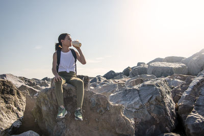 Side view of man standing on rock against sky