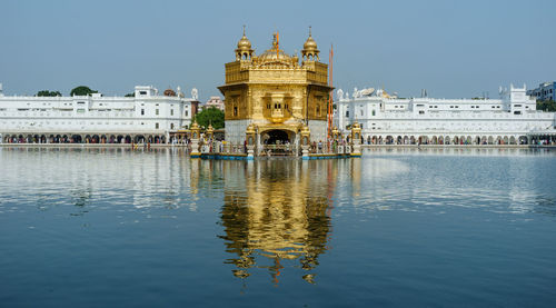 Reflection of golden temple in lake against clear sky