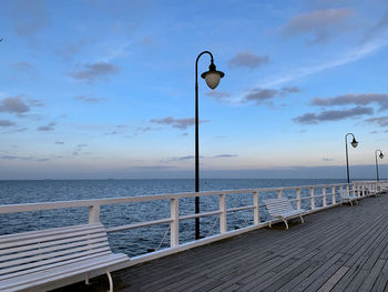 Street lights on pier by sea against sky