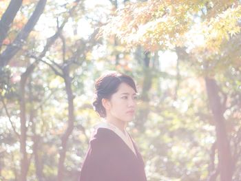 Portrait of young woman standing against trees