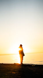 Silhouette woman standing at beach against sky during sunset