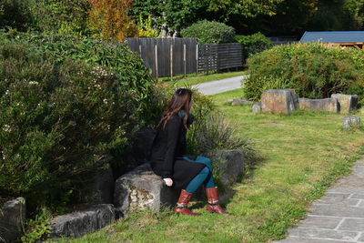 Woman sitting on rock at lawn by footpath