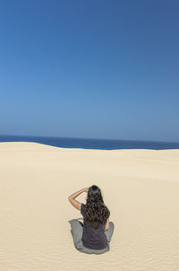 Rear view of woman on beach against clear blue sky