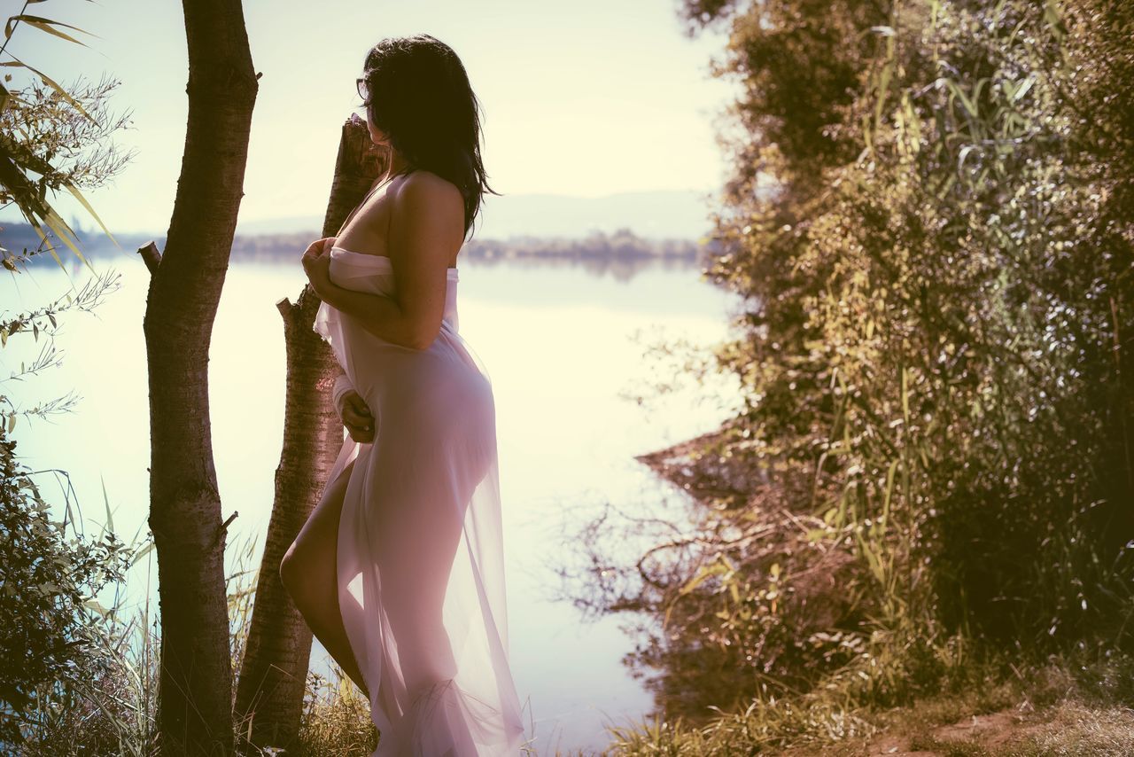 tree, young adult, leisure activity, lifestyles, standing, young women, looking down, lake, long hair, person, getting away from it all, non-urban scene, casual clothing, scenics, water, tree trunk, tranquility, tranquil scene, nature, focus on foreground, vacations, beauty, outdoors