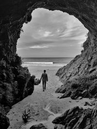 Rear view of man walking on beach against sky