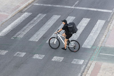 Female delivery person with backpack riding bicycle at crossroad