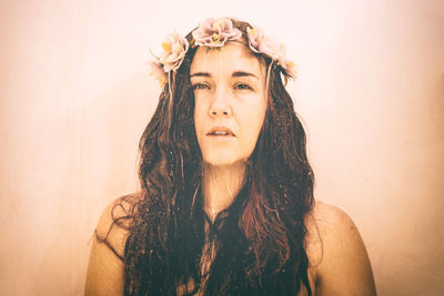 Front view of long haired woman standing against wall with water flowing over her