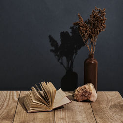 Clay vase with brown dry flowers,natural stone,open old book on wooden table over of black  backdrop