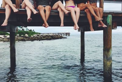 Low section of female friends sitting over sea on pier