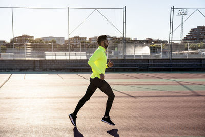 Male athlete jogging on running track at sports court during sunny day