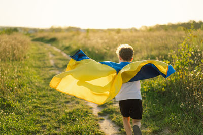 Ukrainian child boy in white t shirt with yellow and blue flag of ukraine in field.