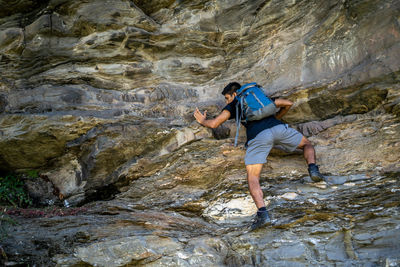 Young boy climbing the rocks wearing a backpack.