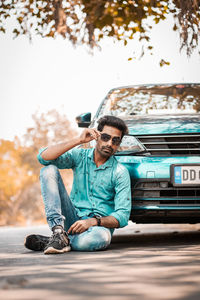 Portrait of young man in sunglasses sitting by car