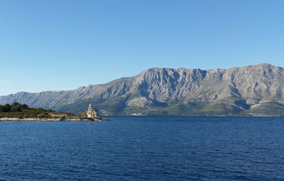 Scenic view of sea and mountains against clear blue sky