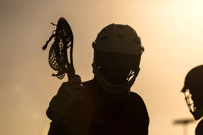 Silhouette lacrosse players against sky during sunset