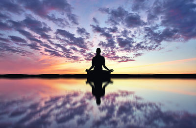 Silhouette woman reflecting in lake while doing yoga at sunset