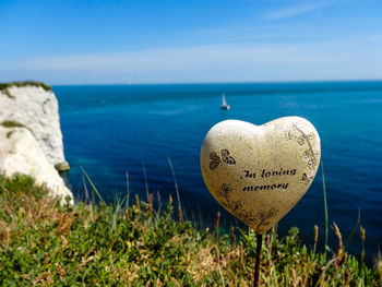 Close-up of heart shape by sea against blue sky