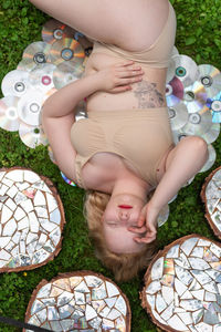 Top view portrait of a young woman lying on a lawn among stumps covered with a mirror