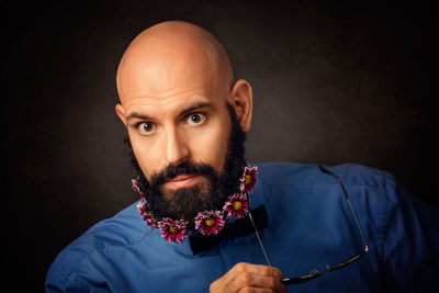 Portrait of hipster with flowers in beard against black background