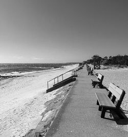 Empty benches on beach against clear sky in black and white 