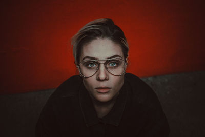 Portrait of young woman wearing eyeglasses against red wall