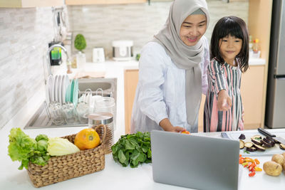 Full length of woman standing by food in kitchen