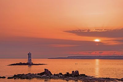 Lighthouse by sea against sky during sunset