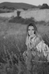 Beautiful young woman posing seated and looking straight ahead in a field of lavender blossoms