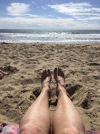 Low section of woman relaxing at beach against sky