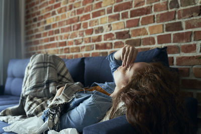 Rear view of woman sitting against brick wall