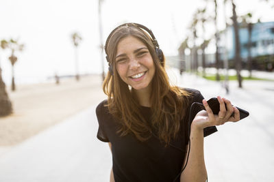 Portrait of happy young woman on boardwalk listening to music