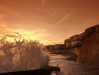 Wave splashing on pier against sky during sunset