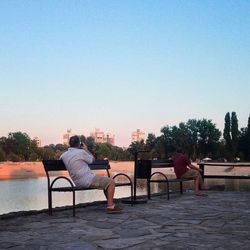 People sitting on bench against clear sky