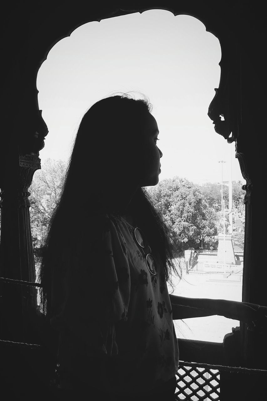 SIDE VIEW OF YOUNG WOMAN LOOKING AT WINDOW