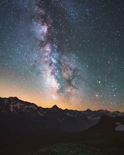 Star field galaxy glowing over snowcapped mountain