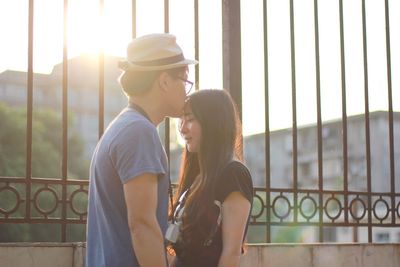 Young man kissing girlfriend while standing by fence