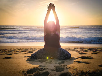 View of woman doing yoga at beach against sky during sunset