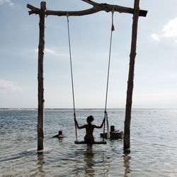 Rear view of man standing on swing at sea