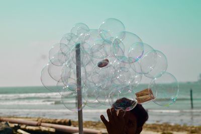 Person holding bubbles over sea shore against sky