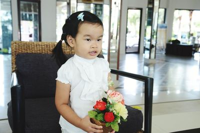 Cute girl holding plant while sitting on chair at home