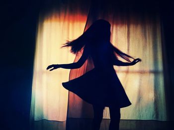 Silhouette woman spinning in dark against illuminated window at home