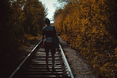 Rear view of woman walking on railroad tracks amidst trees