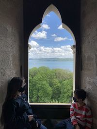 Rear view of people by sea against sky seen through window