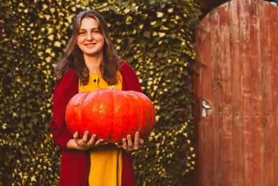 Portrait of smiling young woman standing by pumpkin