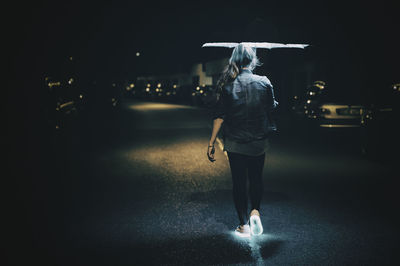 Rear view of woman walking with glowing shoes on street at night