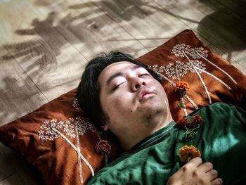 High angle portrait of man lying on brown cushion and holding yellow, marigold flower.