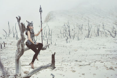 Woman with sword sitting on branch during winter