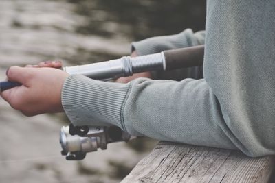 Midsection of man holding camera while sitting on wood