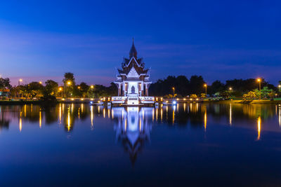 Illuminated building by lake against sky at dusk
