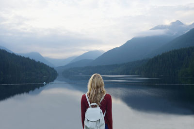 Rear view of woman standing by lake against sky